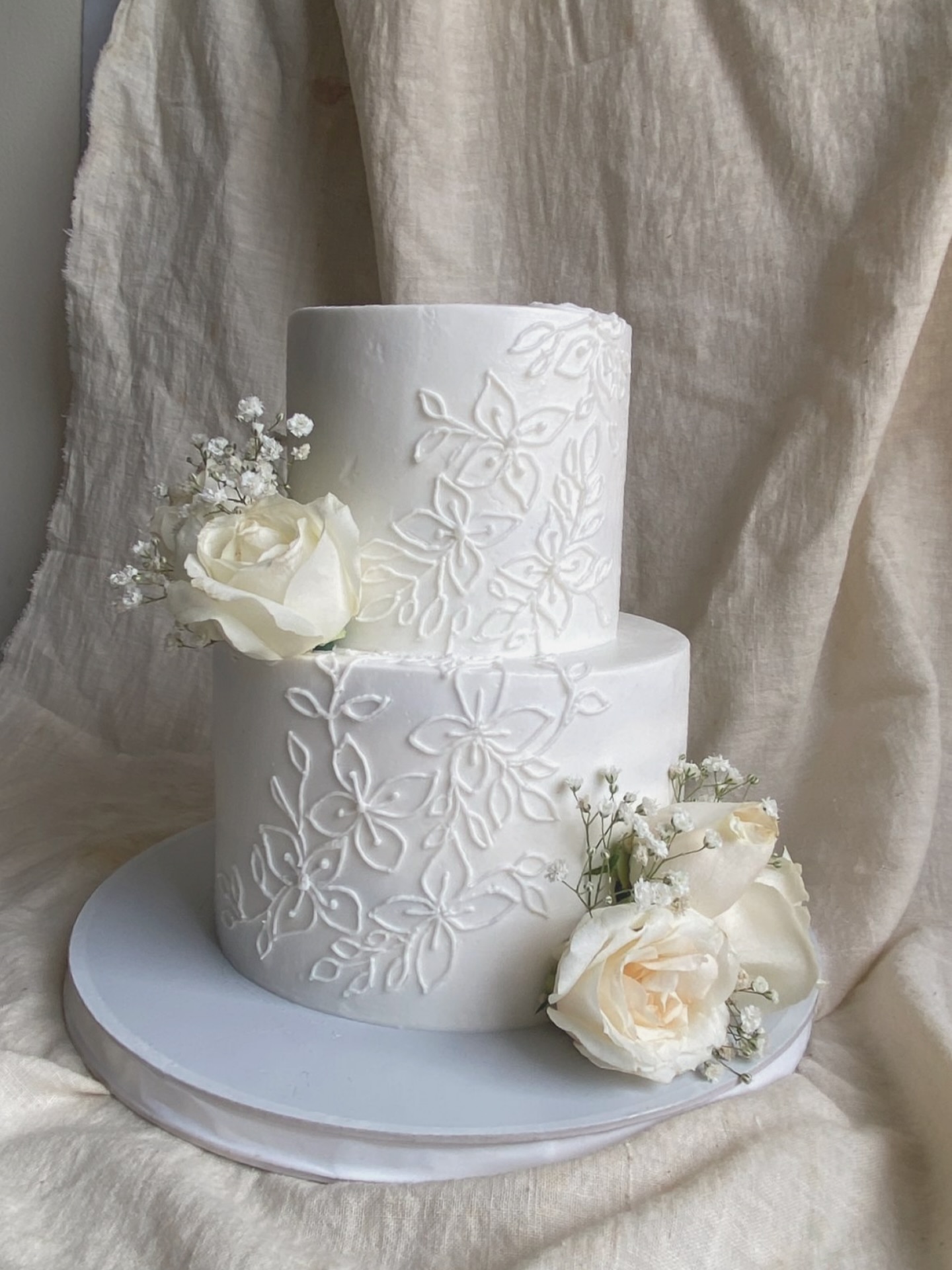 Two-tier wedding cake with hand-piped lace detailing and fresh roses