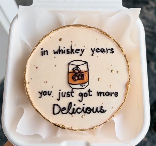 Whiskey-themed birthday cake with hand-piped illustration and gold leaf edge